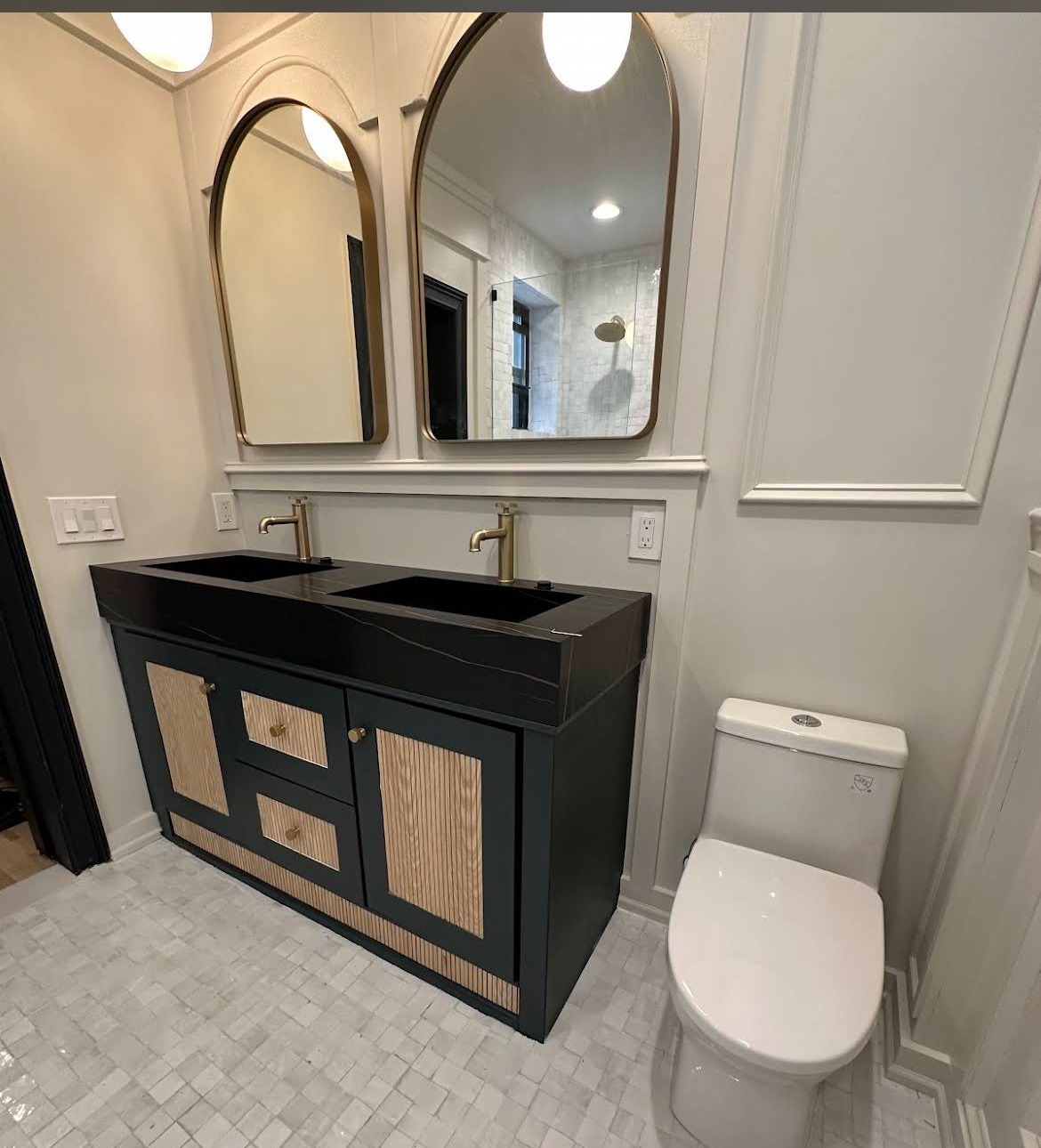 Double vanity with black basins, brass faucets and arched mirrors
